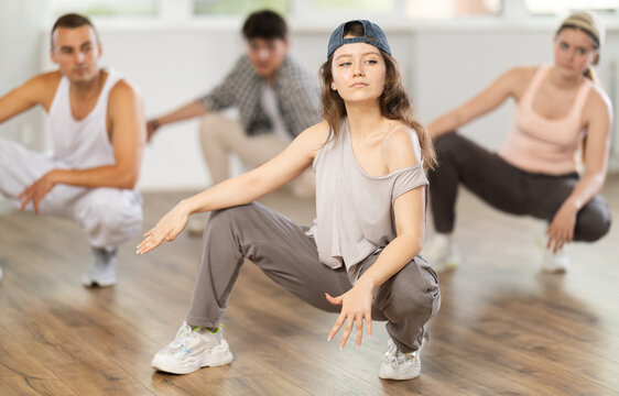 Dynamic young woman training breakdance sitting pose in dancehall during workout session