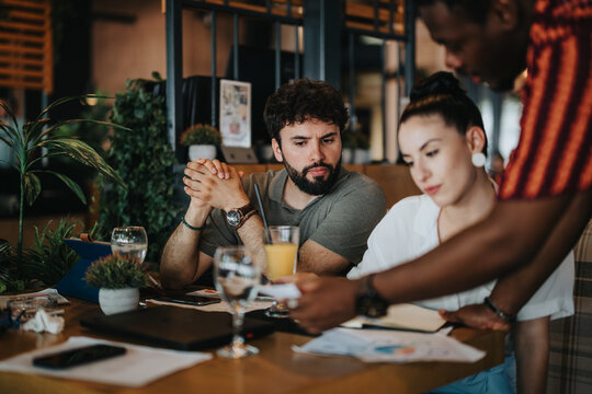 Diverse group of coworkers engaged in a collaborative business meeting at a coffee shop, discussing documents and sharing ideas.
