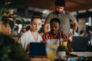 Diverse group of individuals collaborating in a business meeting at a coffee bar, working and discussing ideas.