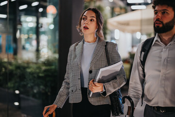 Businesspeople walking in a modern office building lobby at night, holding documents and having a discussion. Professional work environment with focus on business and corporate lifestyle.