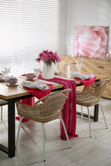 Pink peonies on table with beautiful setting and rattan chairs in dining room