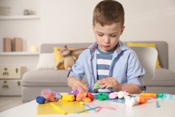 Little boy sculpting with play dough at table in kindergarten