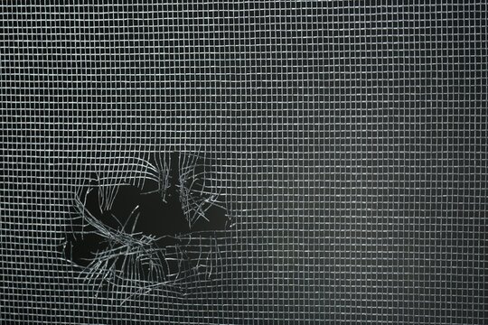 Torn window screen against black background, closeup