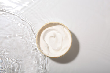 Cosmetic product. Jar with cream in water on light background, top view