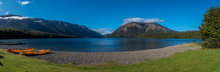 Wide panorama with canoes pulled up on the shore of Lake Rotoiti in Nelson Lakes National Park, New Zealand. Lake and mountains in the background.
