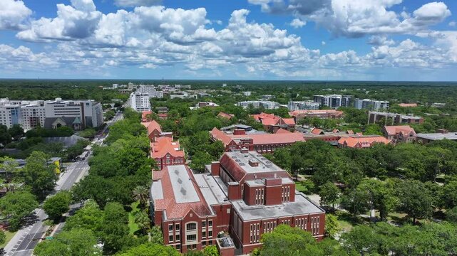 University of Florida Buildings with red brick facade. Drone orbit shot of college campus in Gainesville, Florida, FL, USA. Sunny day with puffy clouds and green trees.	