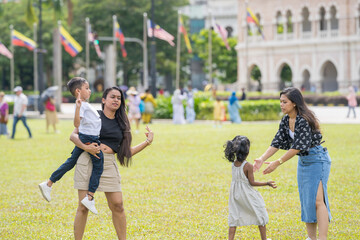 Two thirty-something Indian Malaysian mothers and their seven-year-old son and five-year-old daughter playing joyfully on the expansive lawn at Merdeka Square in Kuala Lumpur, Malaysia.