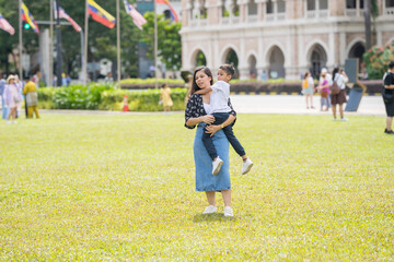 Obraz premium A 30-something Indian Malaysian mother joyfully playing on the expansive lawn at Merdeka Square in Kuala Lumpur, Malaysia, while holding her 7-year-old son.