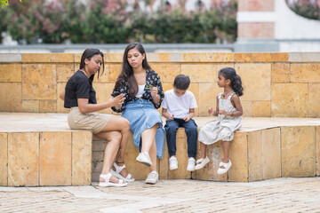 Fototapeta premium Two 30-something Indian Malaysian mothers with their 7-year-old son and 5-year-old daughter spending time joyfully in a historic cobblestone park in City Centre, Kuala Lumpur, Malaysia.