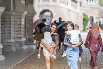 Obraz premium Two 30-something Indian Malaysian mothers with their 7-year-old son and 5-year-old daughter walking happily together in front of a Western-style historical building in Kuala Lumpur, Malaysia.
