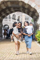 Two 30-something Indian Malaysian mothers with their 7-year-old son and 5-year-old daughter walking happily together in front of a Western-style historical building in Kuala Lumpur, Malaysia.