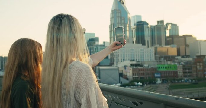 Two young female tourists smile and take selfies in downtown Nashville