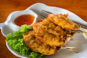 Fried mackerel fish with Crispy fried dough that eat with sauce . Food in the white plate on the wooden table at the seafood restaurant. 