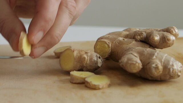Man peeling fresh ginger root on wooden cutting board, close up