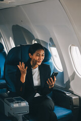 Business woman uses mobile phone and laptop to chat with friends sitting in airplane.