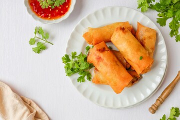 Deep fried vegetable spring rolls or egg rolls and sauce , Thai called popia, in white plate on a white table background with fork
