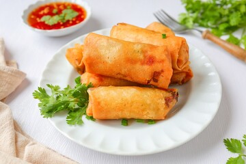 Deep fried vegetable spring rolls or egg rolls and sauce , Thai called popia, in white plate on a white table background with fork