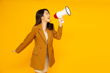 Young Asian businesswoman in yellow suit holding megaphone isolated on yellow studio background, Speech and announce concept