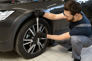 Mechanic in black gloves using a wrench to fix car tire. Man repairing vehicle in modern auto...