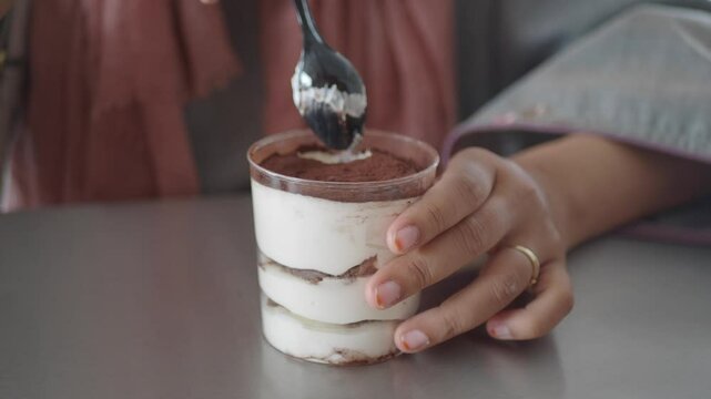 A closeup view of a persons hand grasping a tasty multilayered dessert in a cup