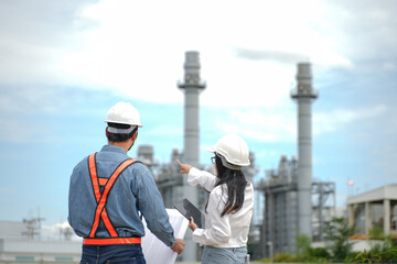Engineers team Reviewing drawing and Plans on Construction Site at Industrial Power Plant. Back view.