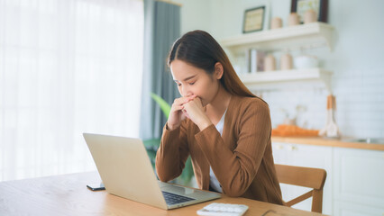 Asian young woman seriously working on computer laptop in house. She thinking find solution problem of work