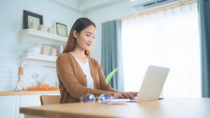 Fototapeta premium Beautiful young Asian woman working with laptop computer in home kitchen. Work at home