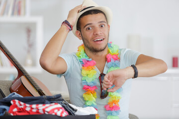 young man packing suitcase looking in shock at wristwatch