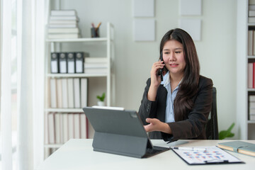 Happy young professional employee sitting at desk with laptop and using mobile phone to contact customers in office using online computer technology startup business idea.