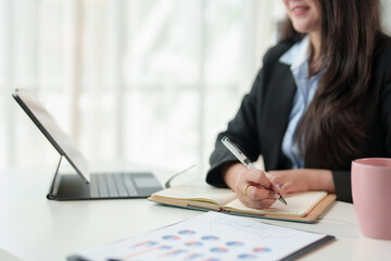 Female office worker, businesswoman writing Recorded in a notebook sitting in the office. with laptop and financial file folders Professional and focused workspace.