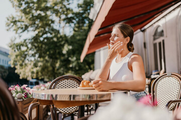 Portrait of happy woman sitting in a cafe outdoor drinking coffee. Woman while relaxing in cafe at table on street, dressed in a white T-shirt and jeans