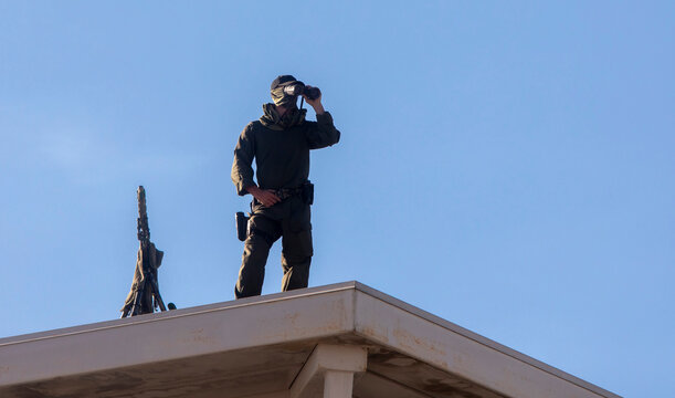 Military sniper on a roof of a building looking through binoculars
