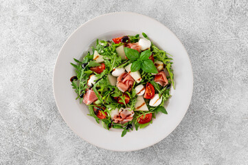 Fresh summer salad with arugula, melon, prosciutto and mozzarella cheese on concrete background, Healthy food. Top view.