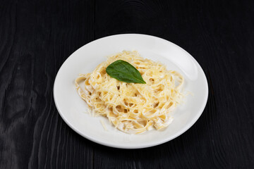 Pasta with sauce and basil in plate on black wooden background