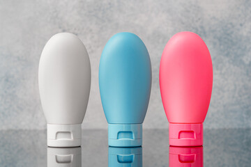 Three Plastic Bottles With White, Blue, and Pink Labels on a Grey Background: Three Plastic Bottles...