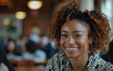 A woman with curly hair is smiling and looking at the camera. She is wearing a black and white shirt and a gold hoop earring