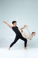 Ballet Dance Ideas. Sportive Couple of Asian Man and Caucasian Woman Performing As Ballet Dancers On Grey in Studio During Suppots As Classical Dance © danmorgan12