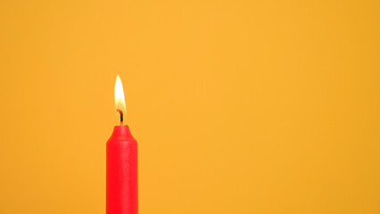 A single red candle burns on a plain yellow backdrop, creating a warm and simple visual. Happy birthday or anniversary video in 4K resolution with copy space