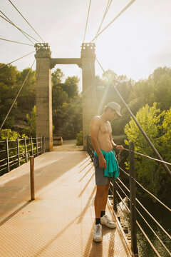 Shirtless sporty guy standing on a bridge over a lake during sunset