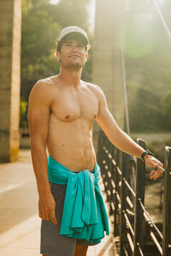 Shirtless sporty guy standing on a bridge over a lake during sunset