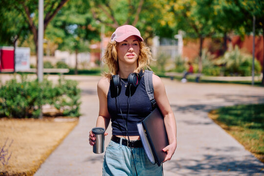 University student walking on campus with coffee and folder