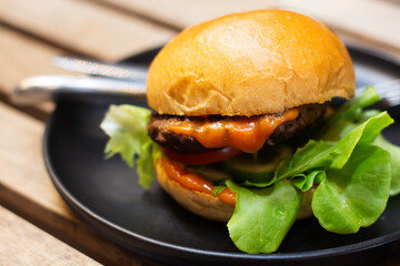 Close-up Hamburger with meat, pickles and ketchup in disk on wooden table.