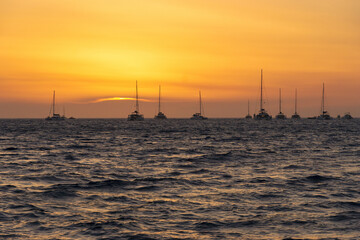 Sunset view of yachts moored on the sea against horizon and yellow glow in the sky, Santorini, Greece
