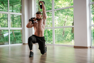 Against the windows. With dumbbells. Strong muscular man is working out in the gym