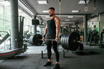 Big and heavy barbell in hands. Strong muscular man is working out in the gym