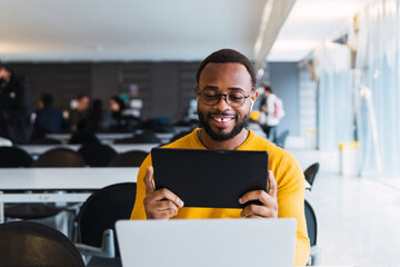 Happy african business man, black male student wearing headphones elearning on laptop in office,...