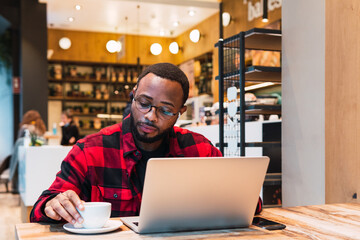 Young african man working on laptop computer in cafe