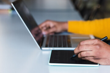 Anonymous black man working on laptop with tablet