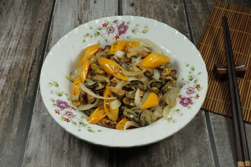 Fried and stirred peeled mussel with yellow chilly pepper and fresh onion serving on the plate. Famous hot and spicy seafood menu in Thai restaurant.
