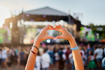 Concertgoer forms heart shape with hands at beachside music festival, crowd enjoys live performance...